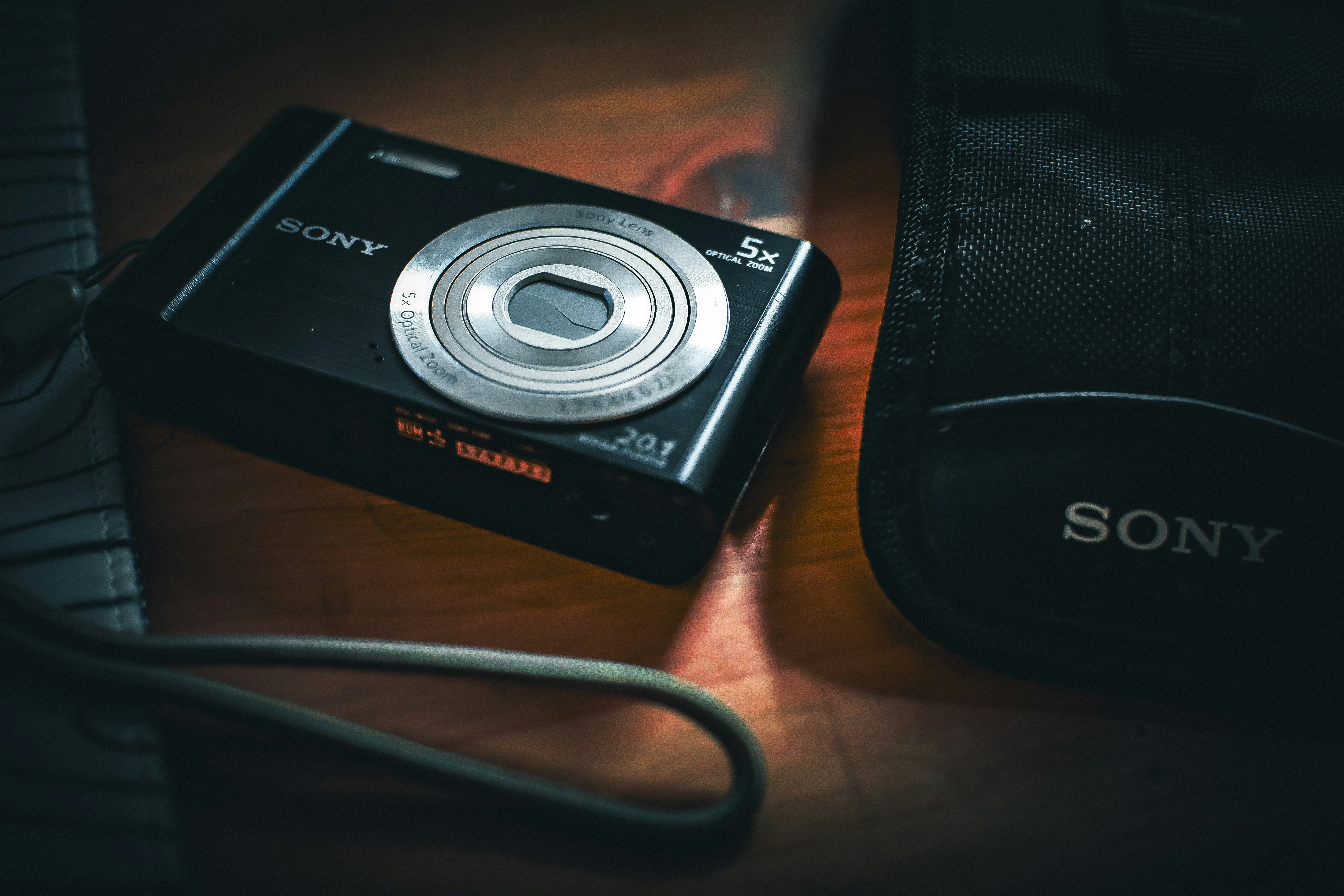 A black sony digital camera lies on a wooden surface.
