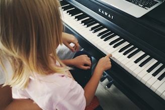 Young girl plays piano with laptop nearby