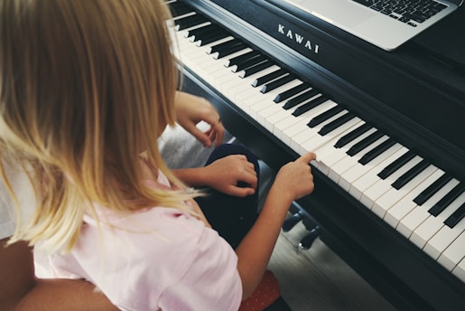 Young girl plays piano with laptop nearby