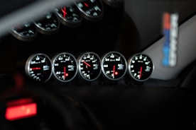 Five car dashboard gauges illuminated at night.