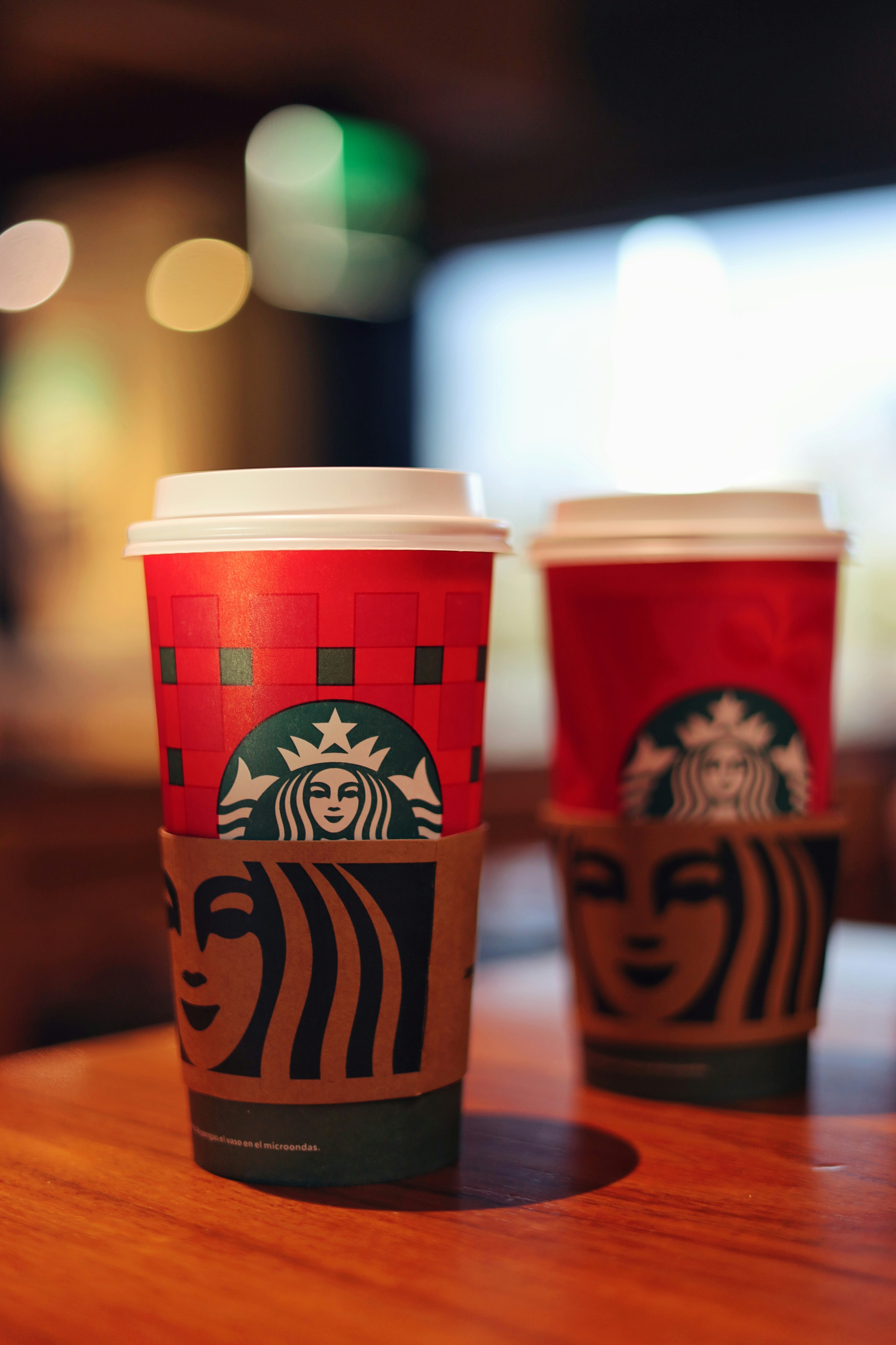 Two starbucks cups with festive red design.