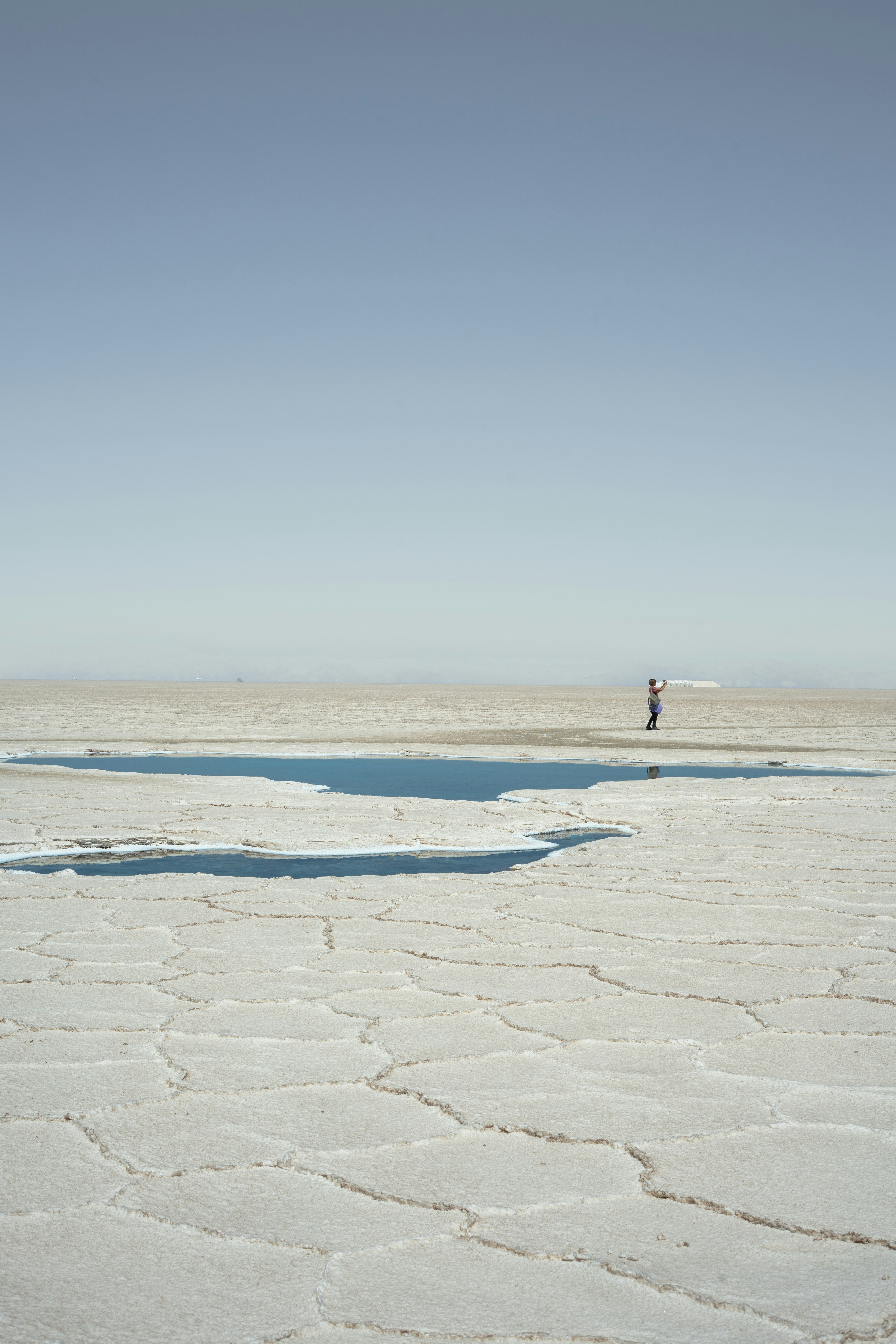 A lone figure stands on a vast, cracked salt flat.