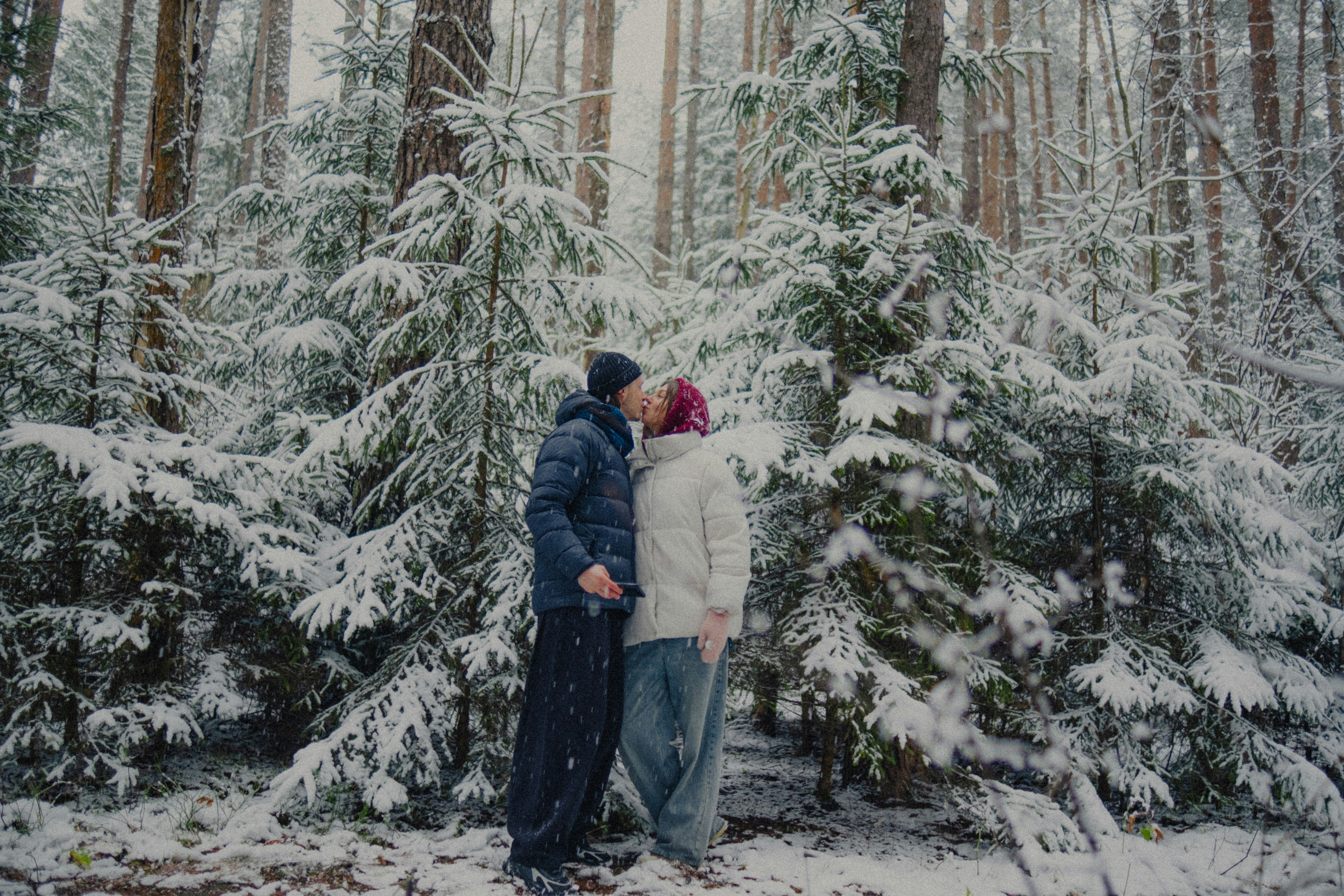 Couple kissing in snowy forest during winter.