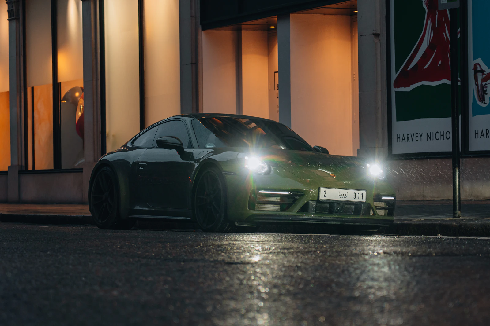 Dark green Porsche 911 on a city street at night with its headlights on