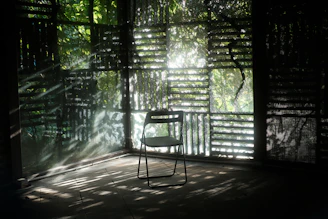 A single chair sits in a sunlit, rustic room.