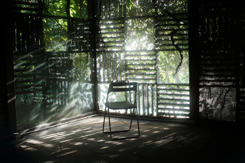 A single chair sits in a sunlit, rustic room.