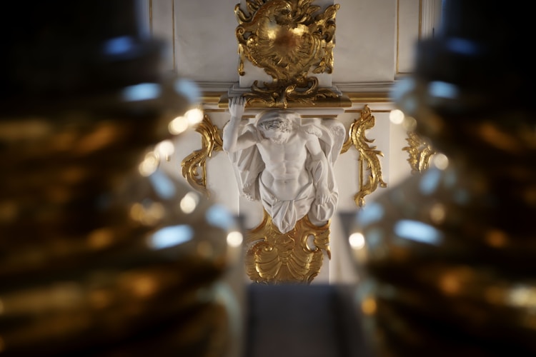 An ornate golden architectural detail beside a white statue, embodying the ancient association between gold and divine perfection