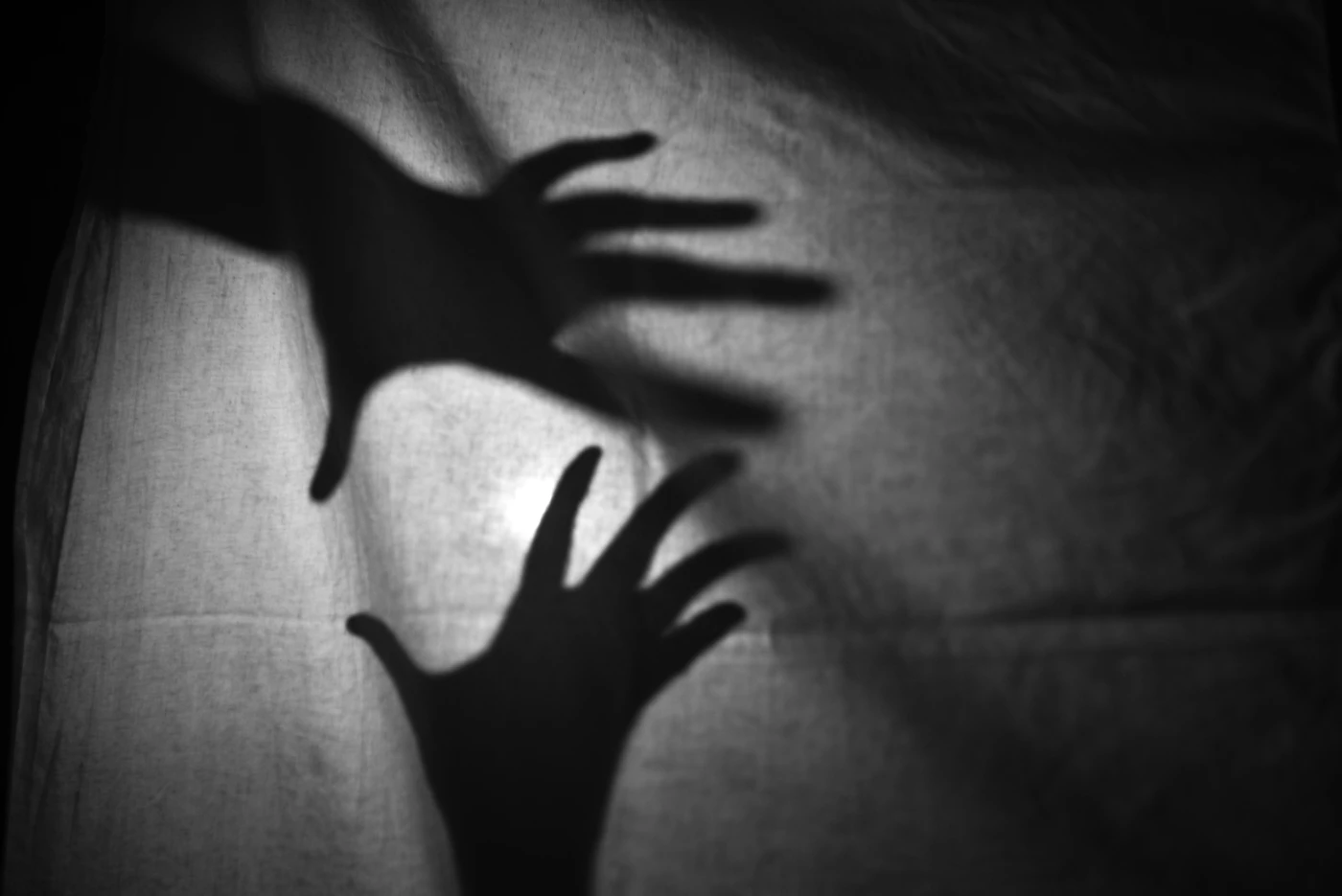 Two hand silhouettes reaching across softly lit fabric