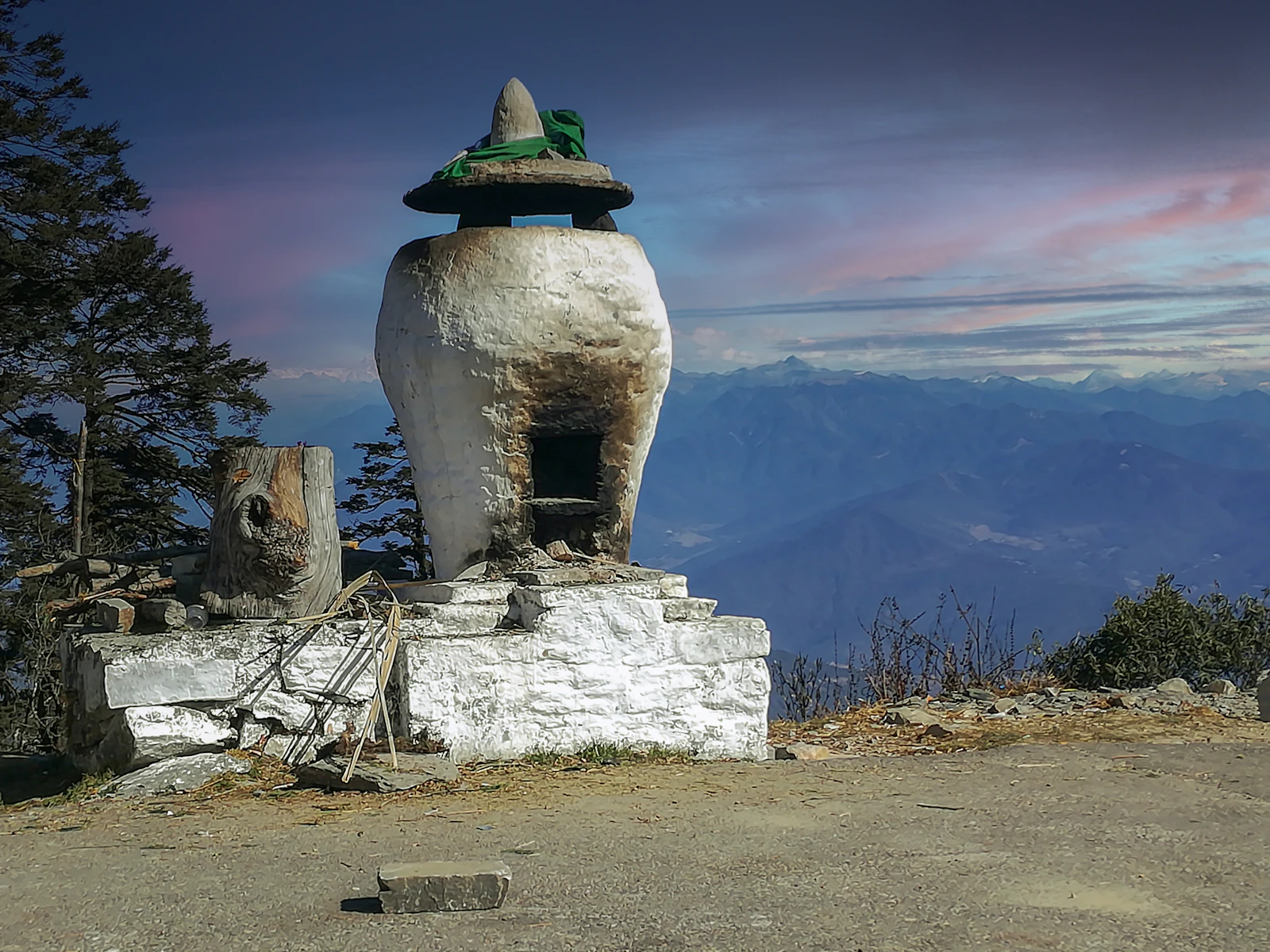 A whitewashed stone chorten on the Dochu La overlook, blue Himalayan ranges fading into the evening sky beyond