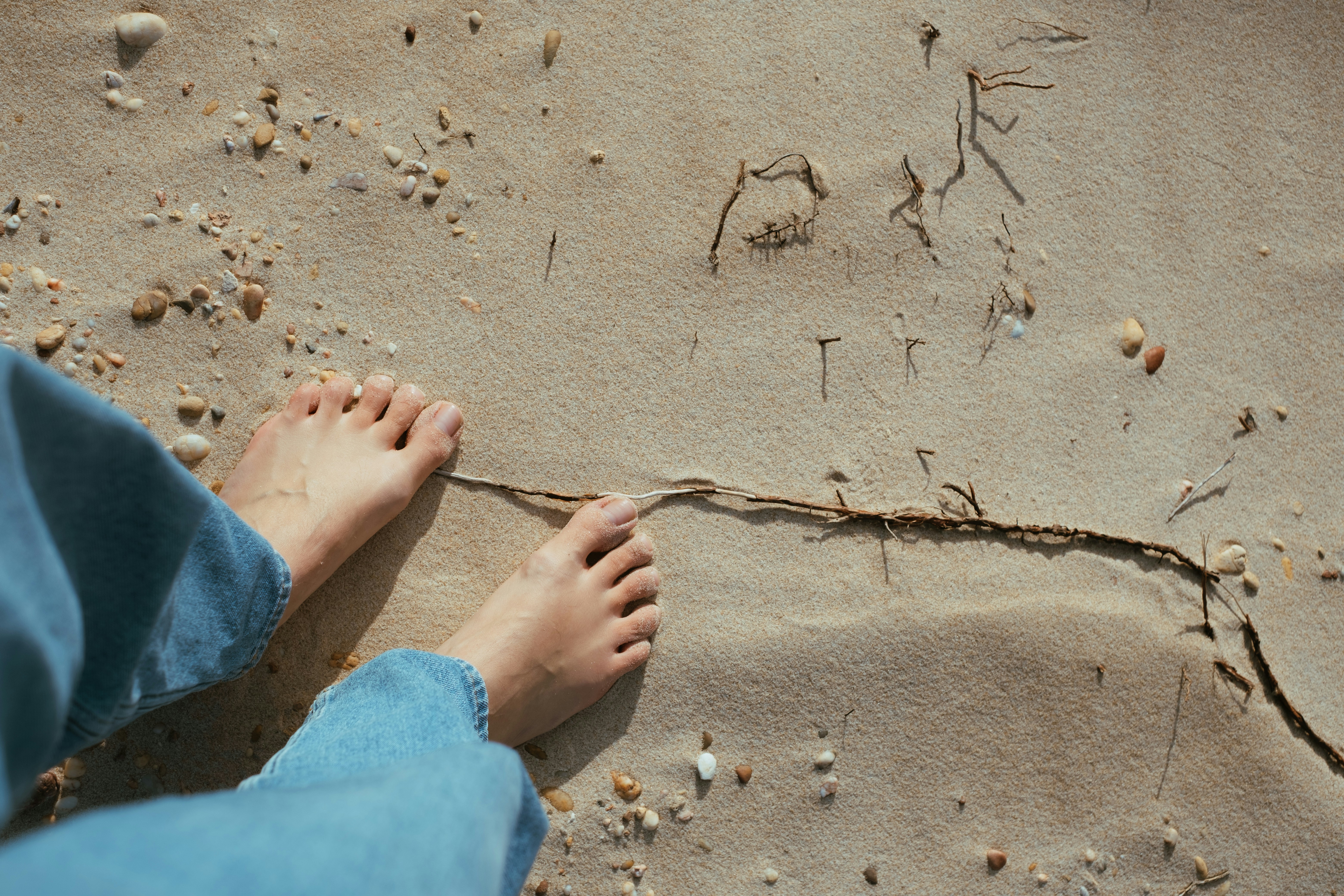 Bare feet on a sandy beach with small shells