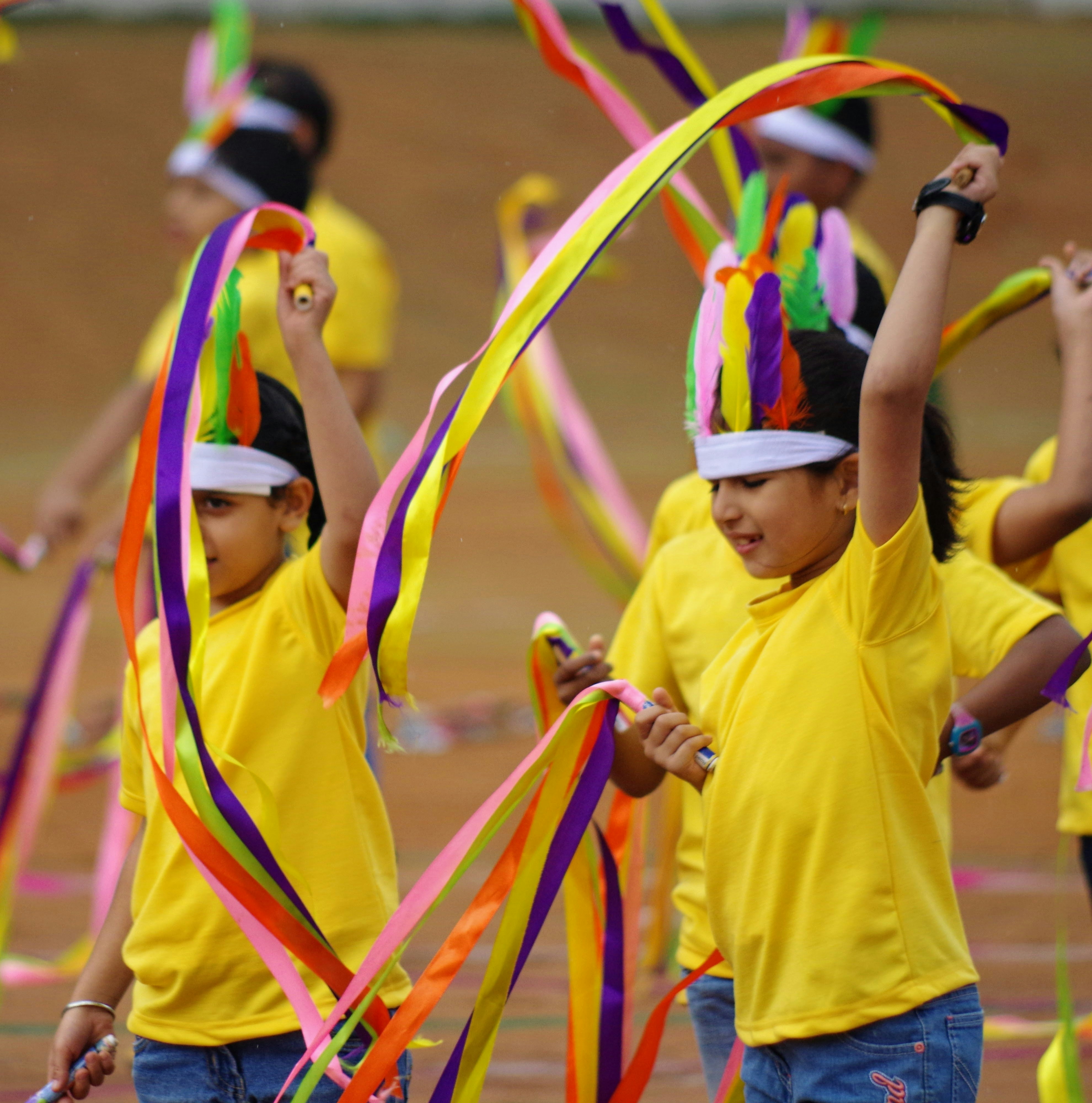 Children in yellow shirts dance with colorful ribbons