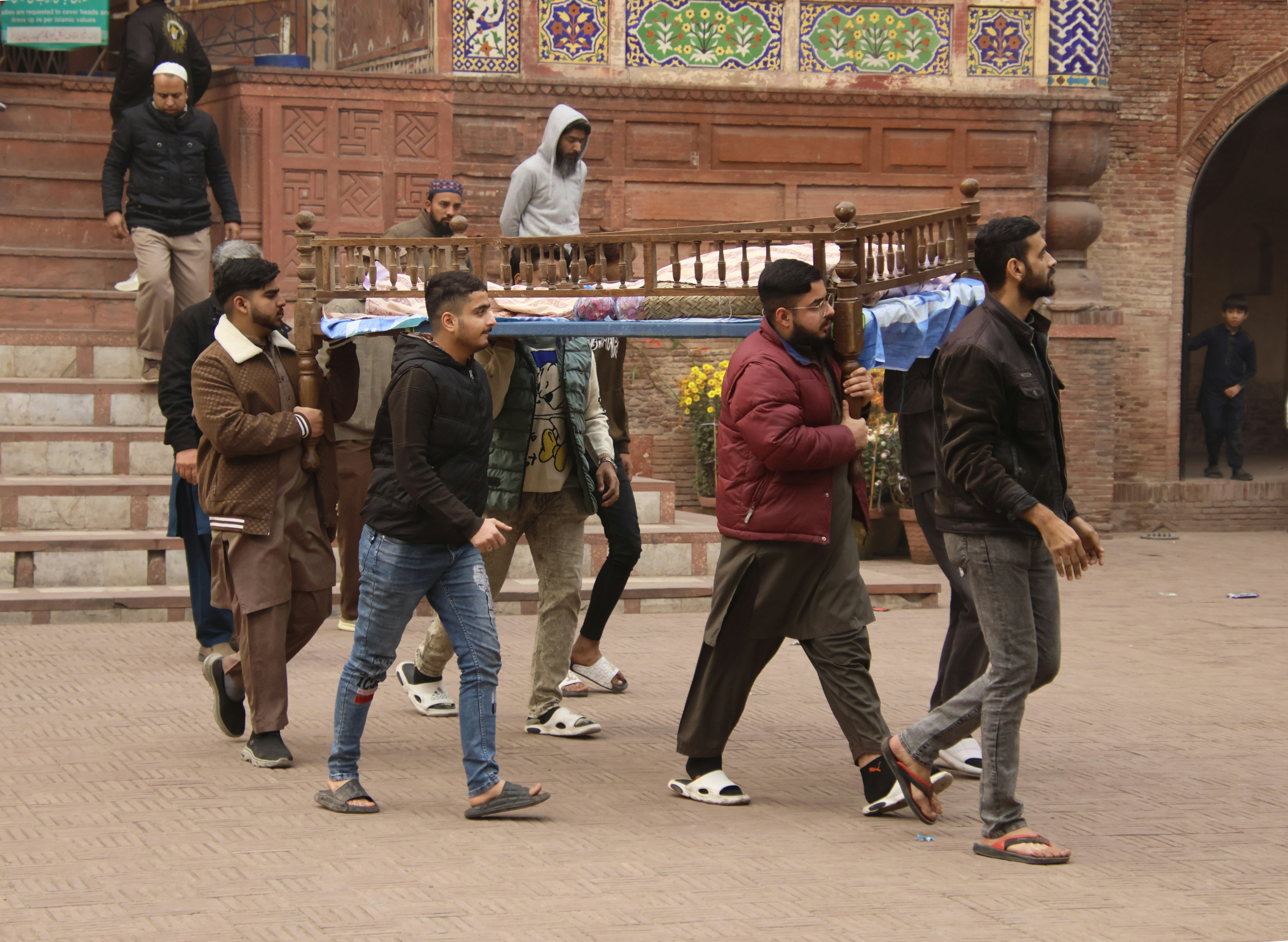 Men carrying a decorated stretcher in a courtyard.