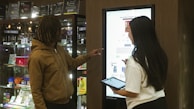Two people interact with a digital display screen.