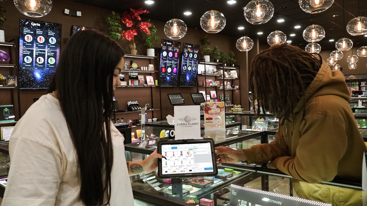Dispensary staff and customer reviewing a tablet at the counter as automated compliance checks run during checkout