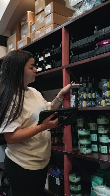 Operadora en almacén con tableta ruggedizada revisando inventario en anaquel — escena de operaciones para análisis causa-efecto