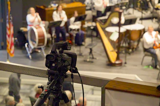 A camera records a live orchestra performance on stage.