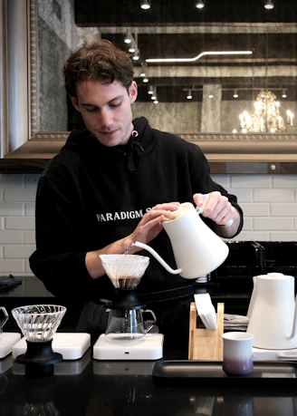 Barista carefully pouring hot water into coffee dripper.