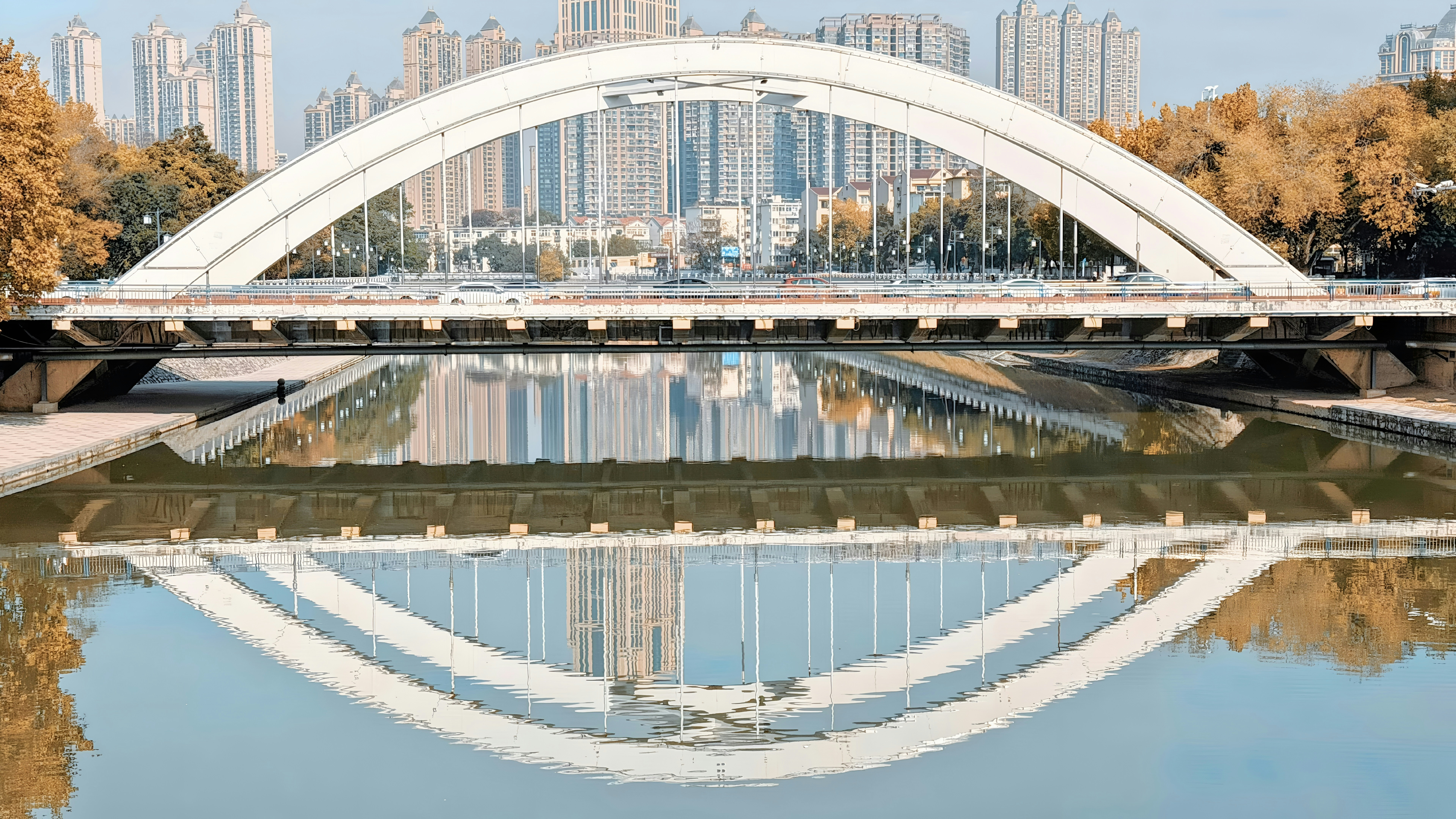 A white arch bridge reflected in calm water.