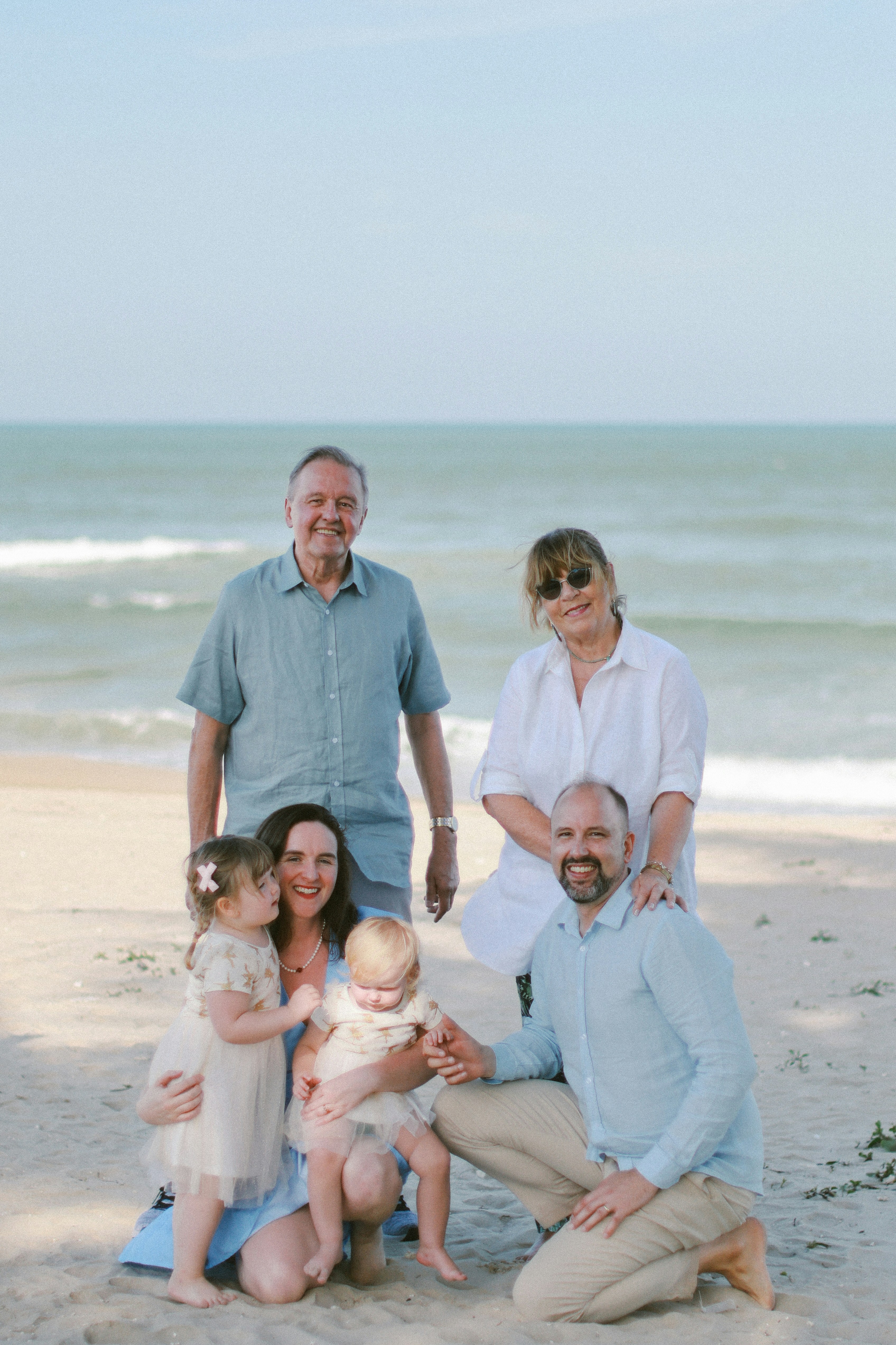 Family posing for a portrait on a sandy beach.