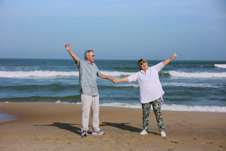 Elderly couple holding hands on a sandy beach.