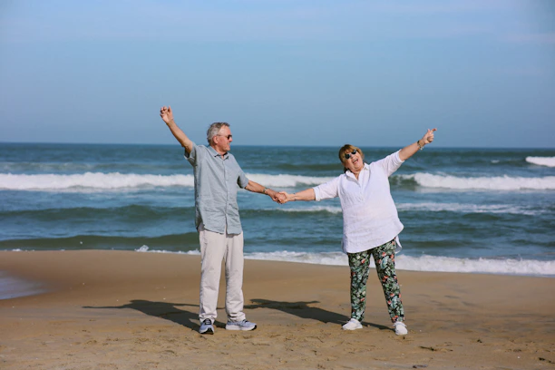 Elderly couple holding hands on a sandy beach.