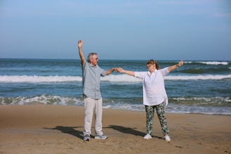 Elderly couple dancing on a beach with ocean waves.