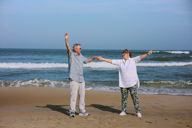 Elderly couple dancing on a beach with ocean waves.