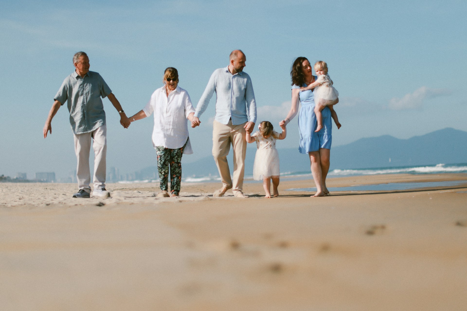 A multi-generational family walks on a sandy beach.