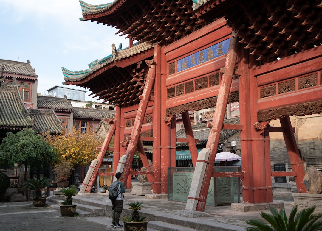 Man stands before a large red traditional chinese gate.