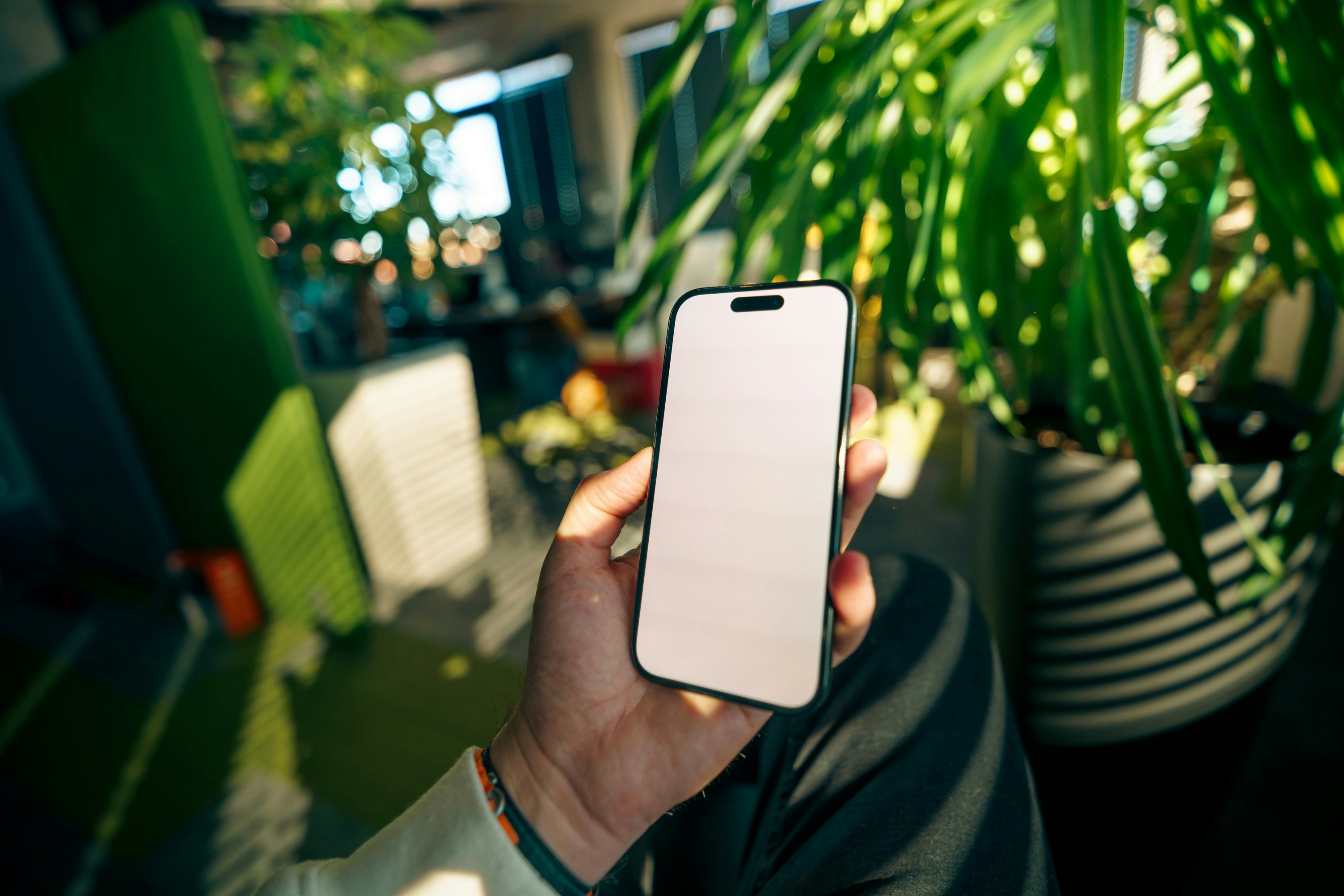 Mano sosteniendo un smartphone con pantalla en blanco dentro de casa.
