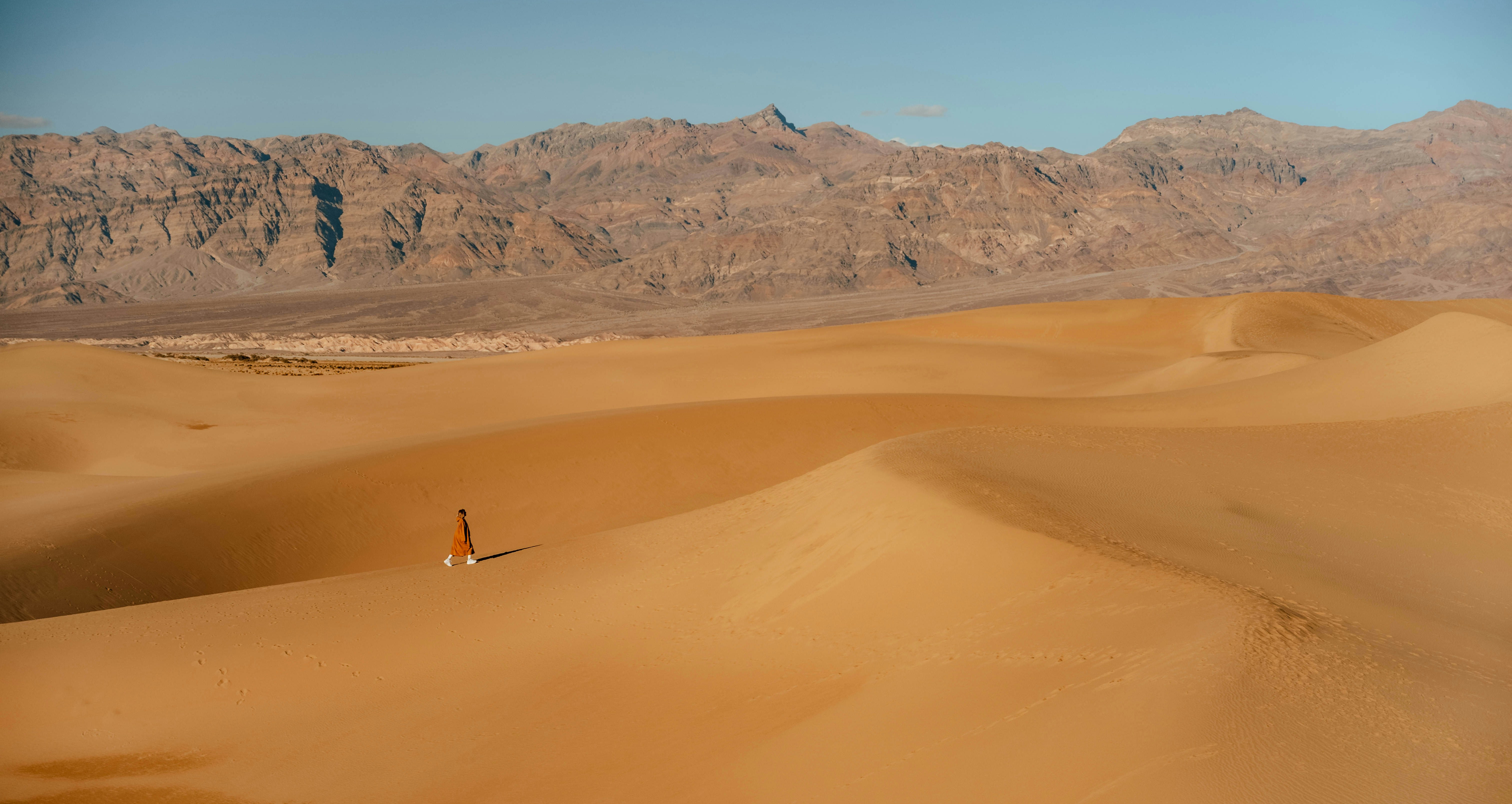 A lone figure walks across vast sand dunes.