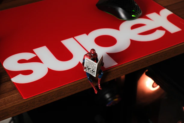 Spider-man figure reading a newspaper on a red mat.
