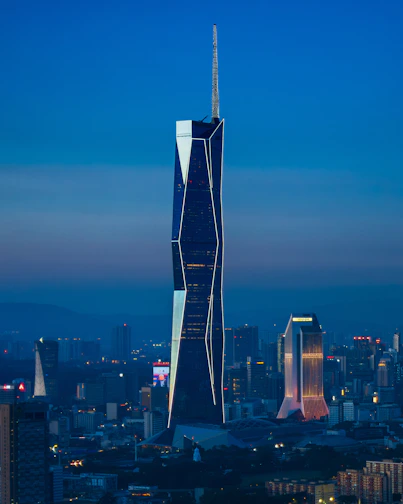 Modern skyscraper illuminated at dusk with city skyline.