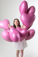 Young woman holding pink heart-shaped balloons