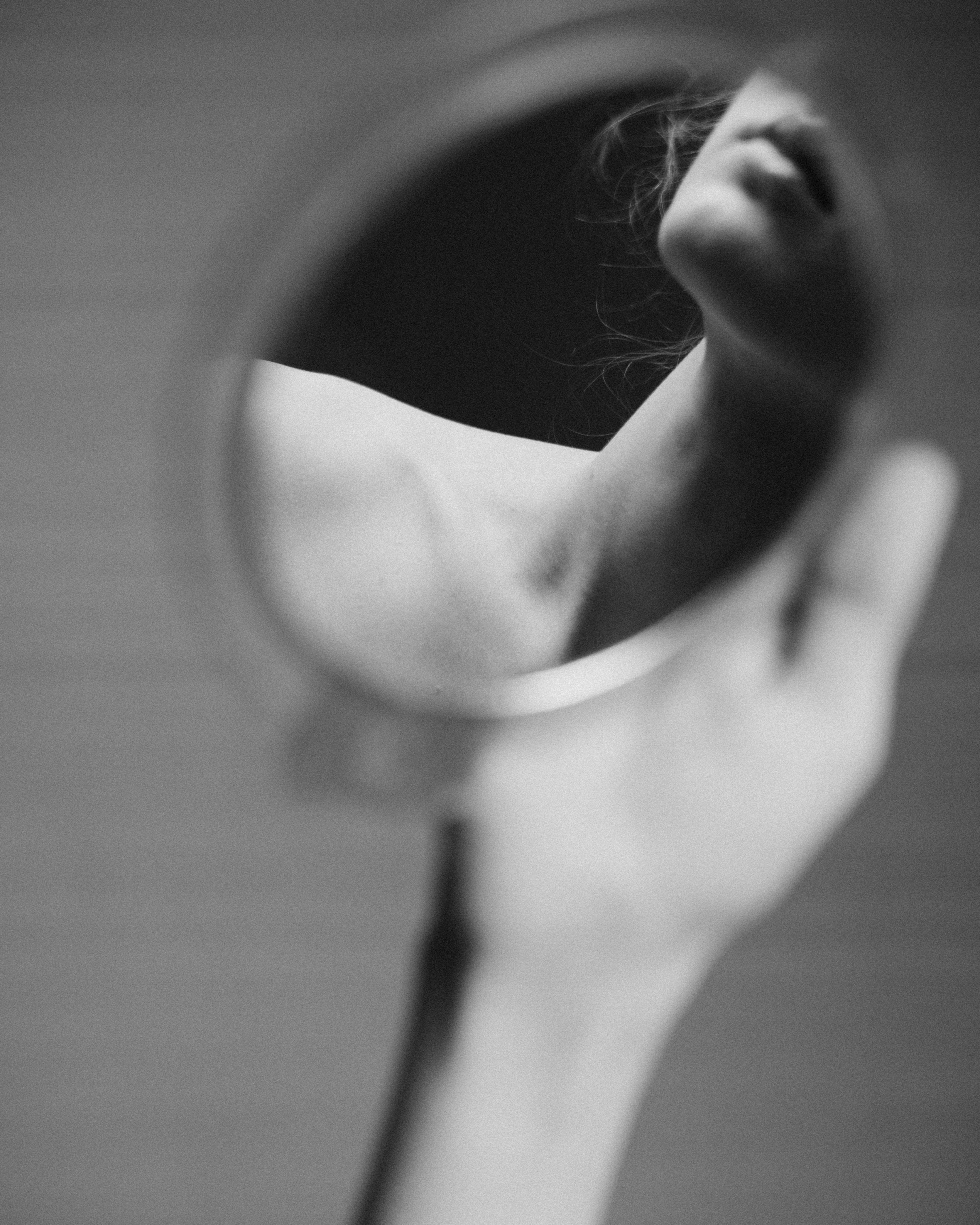 A hand holding a small round mirror reflecting a person's neck and chin