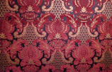 Intricate red and gold paisley pattern on dark background.