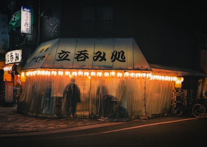 A dimly lit street scene with a glowing japanese restaurant.