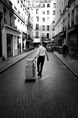 Man pushing boxes on a cart down a cobblestone street.