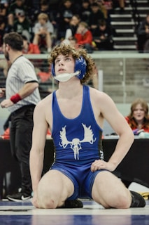 Wrestler in blue singlet with moose logo looks up.