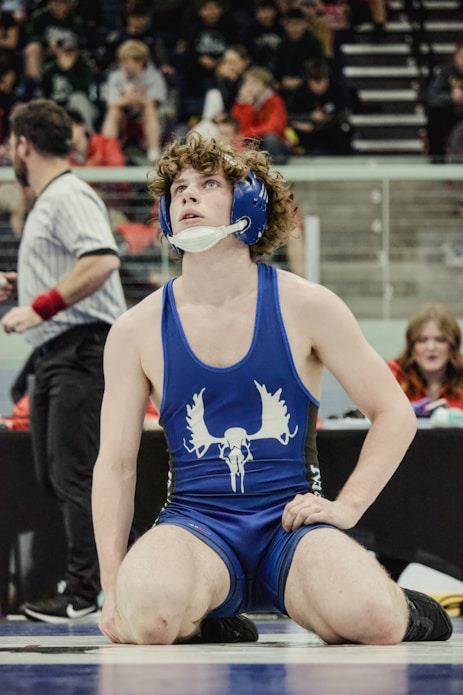 Wrestler in blue singlet with moose logo looks up.