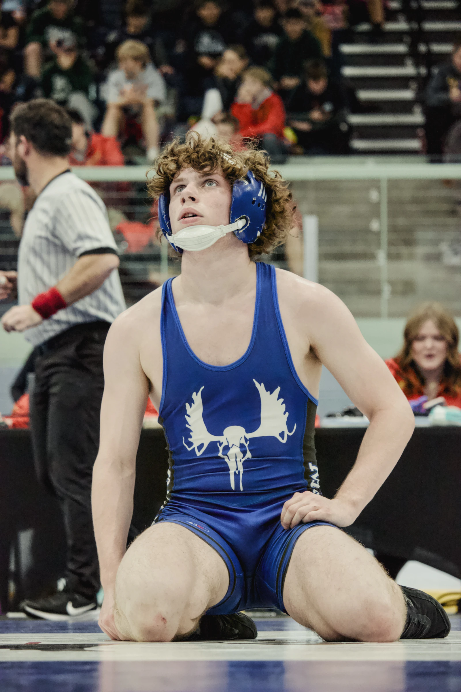 Wrestler in a blue singlet looking up during a match