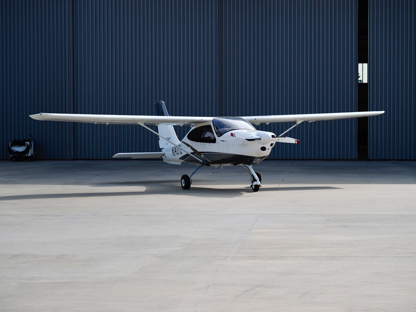 Small white light aircraft parked outside a hangar
