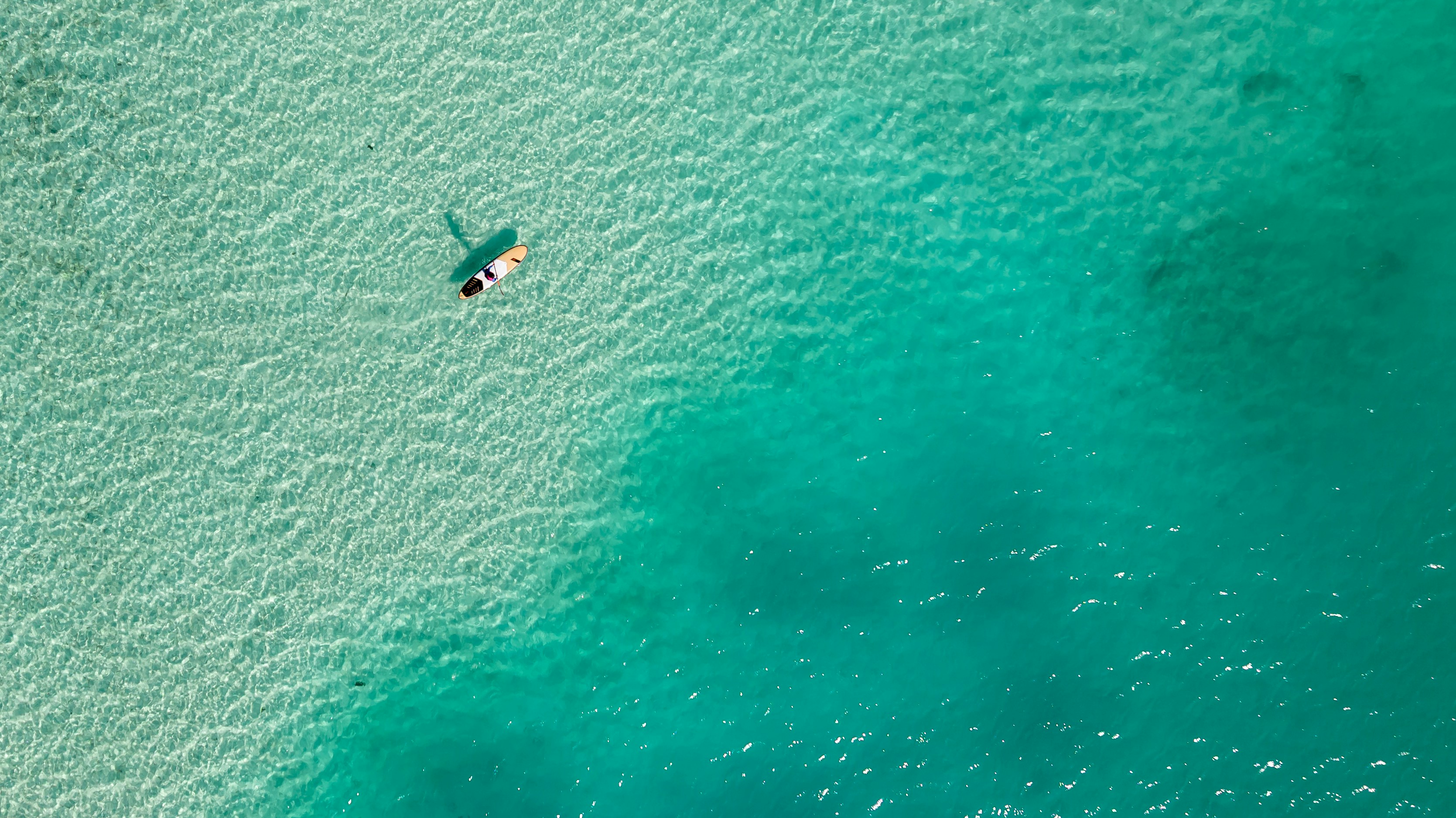 澄んだターコイズ色の水の中でパドルボードに浮かぶ人物。