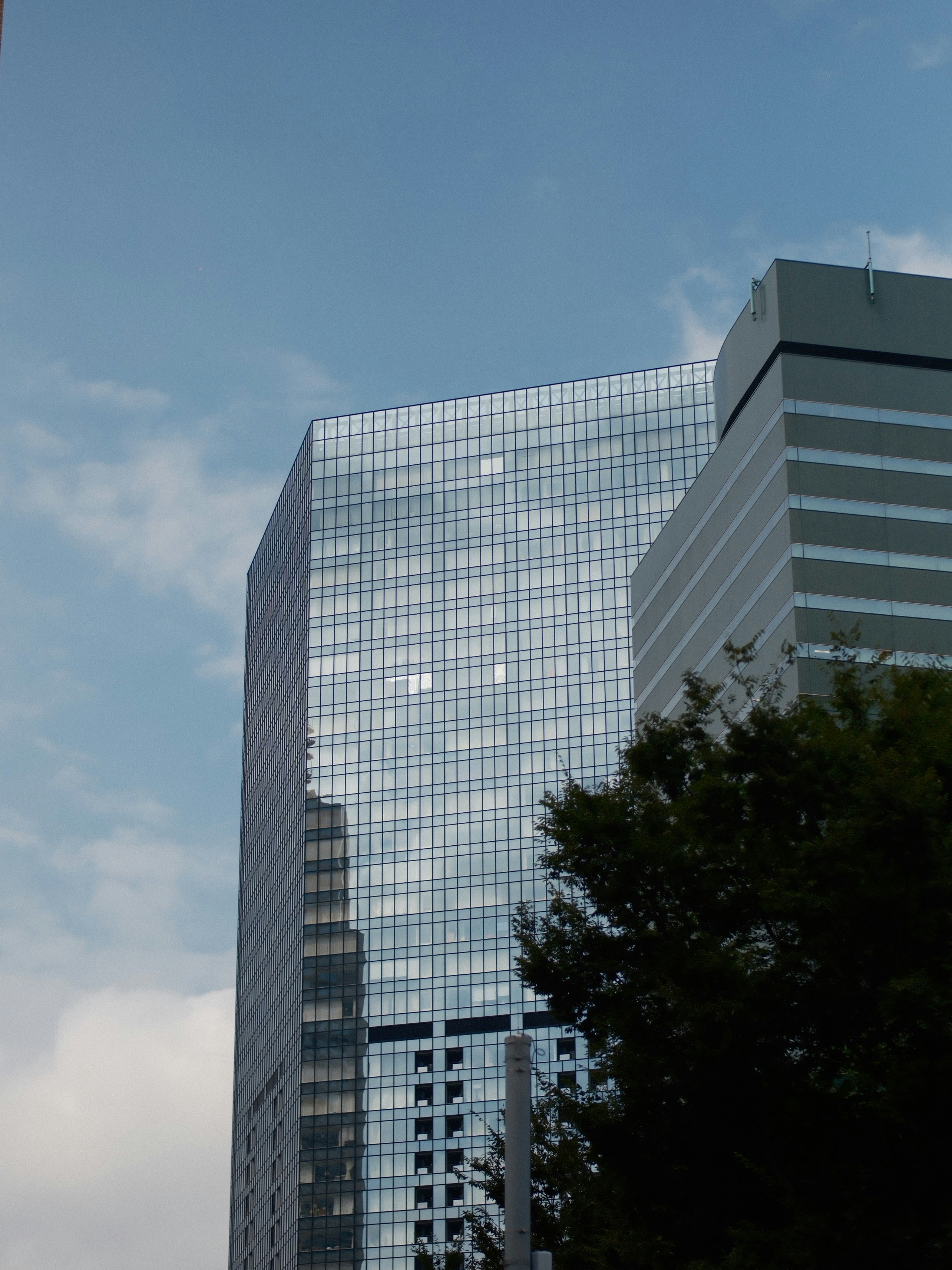 A glass skyscraper reflecting the sky and a nearby building under a blue sky