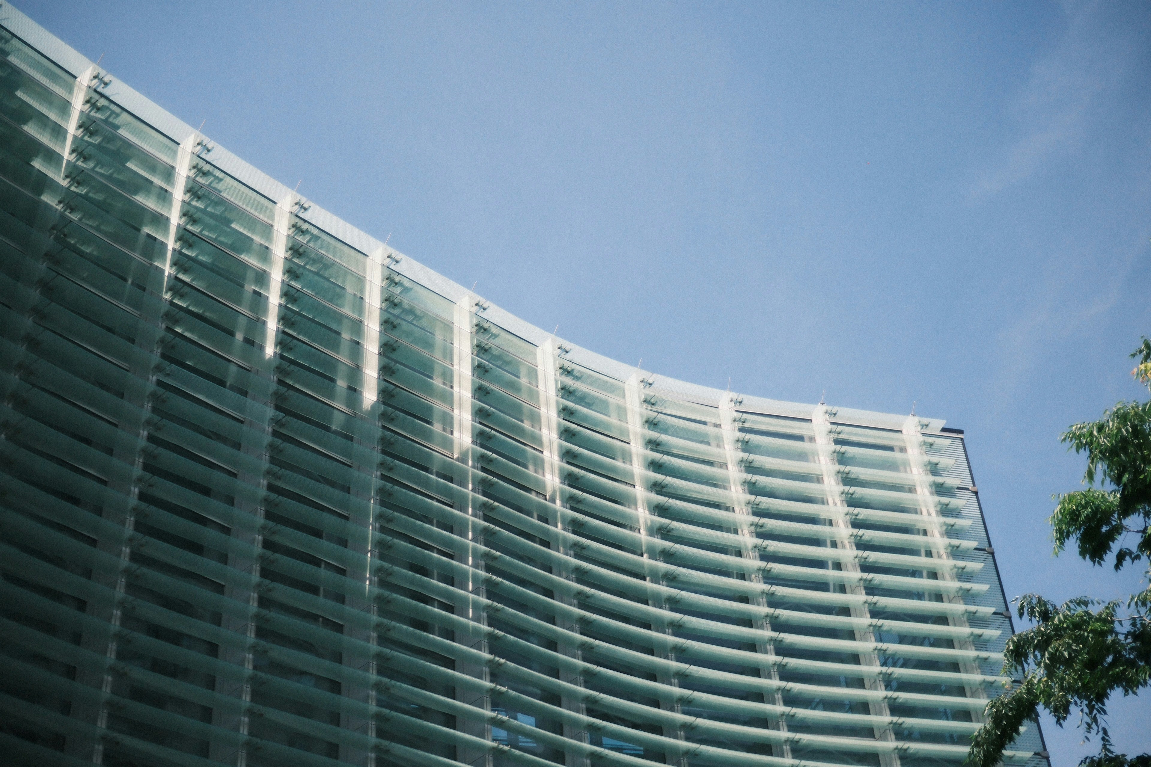A curved glass facade of a modern building against a clear blue sky