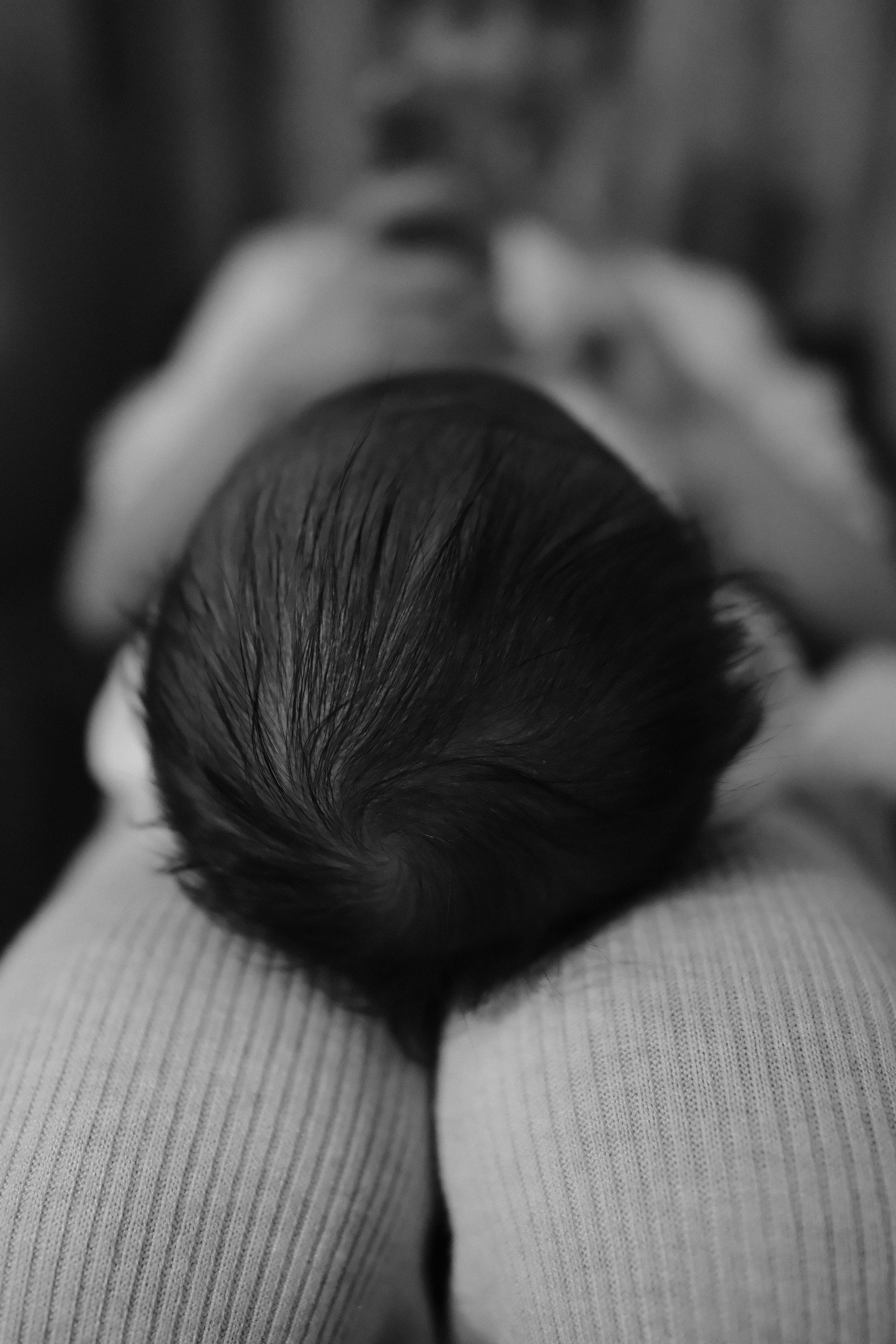 A baby with dark hair resting on a person's lap in black and white