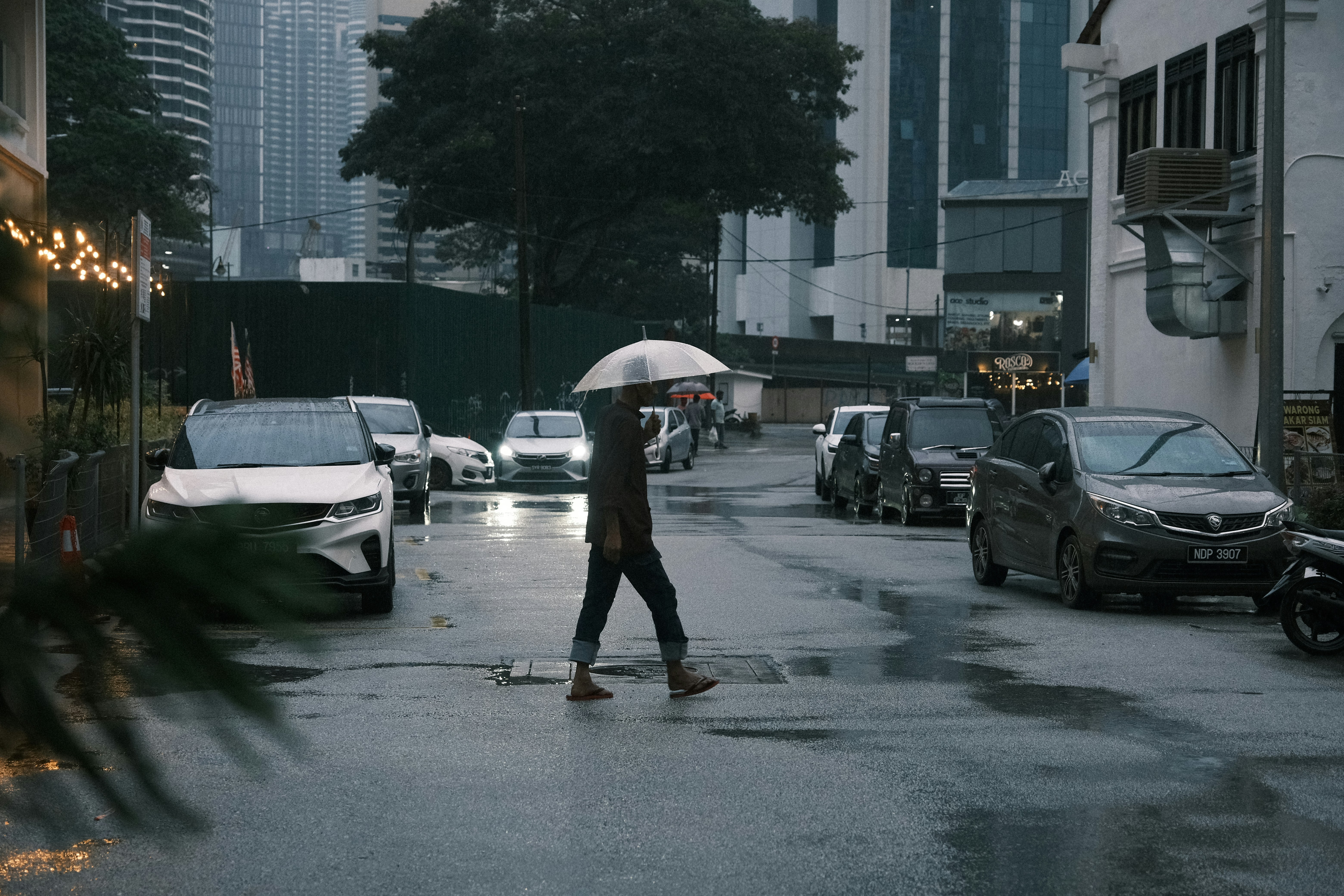 Une personne avec un parapluie traverse la rue mouillée en ville