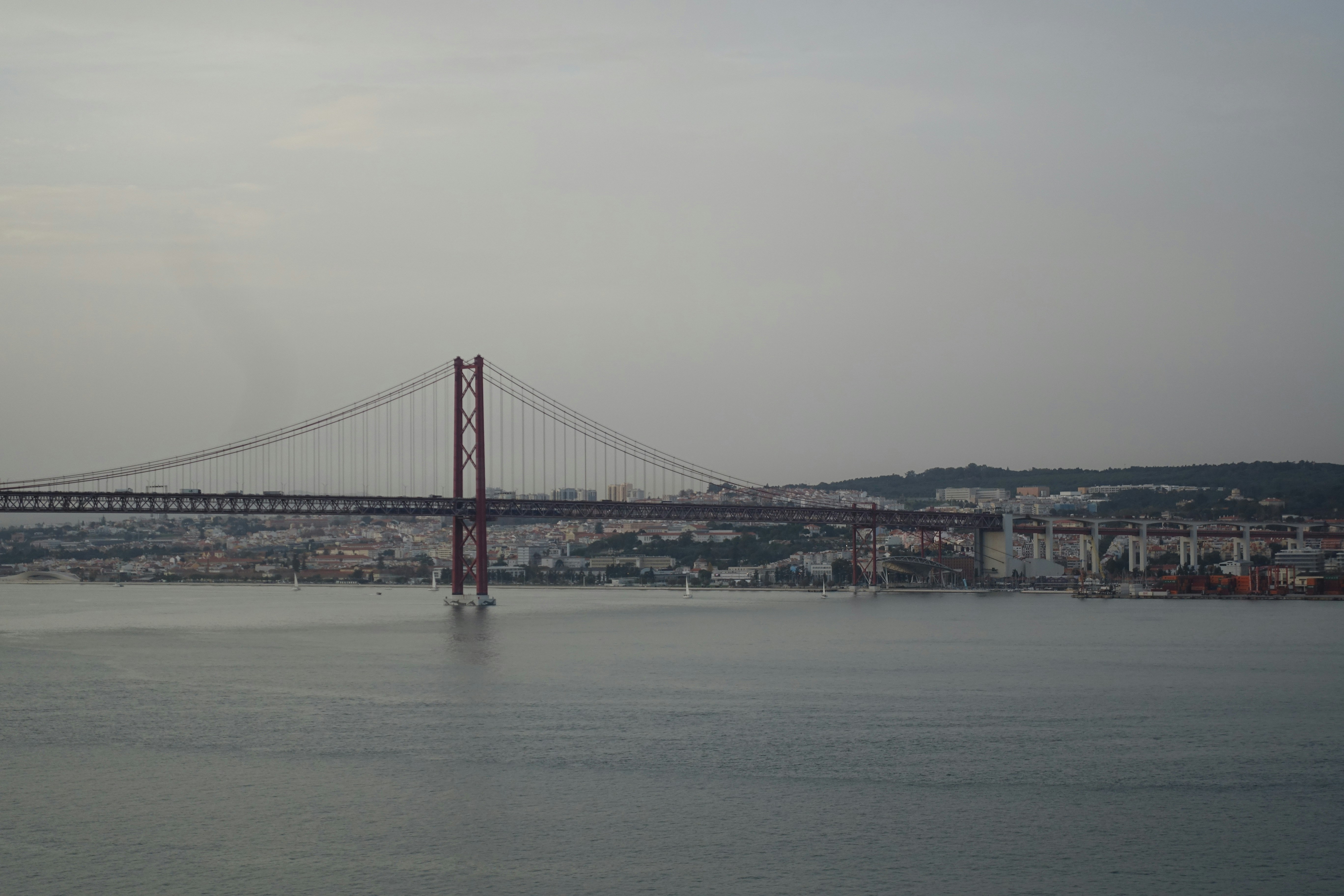 Suspension bridge over a wide river with city skyline
