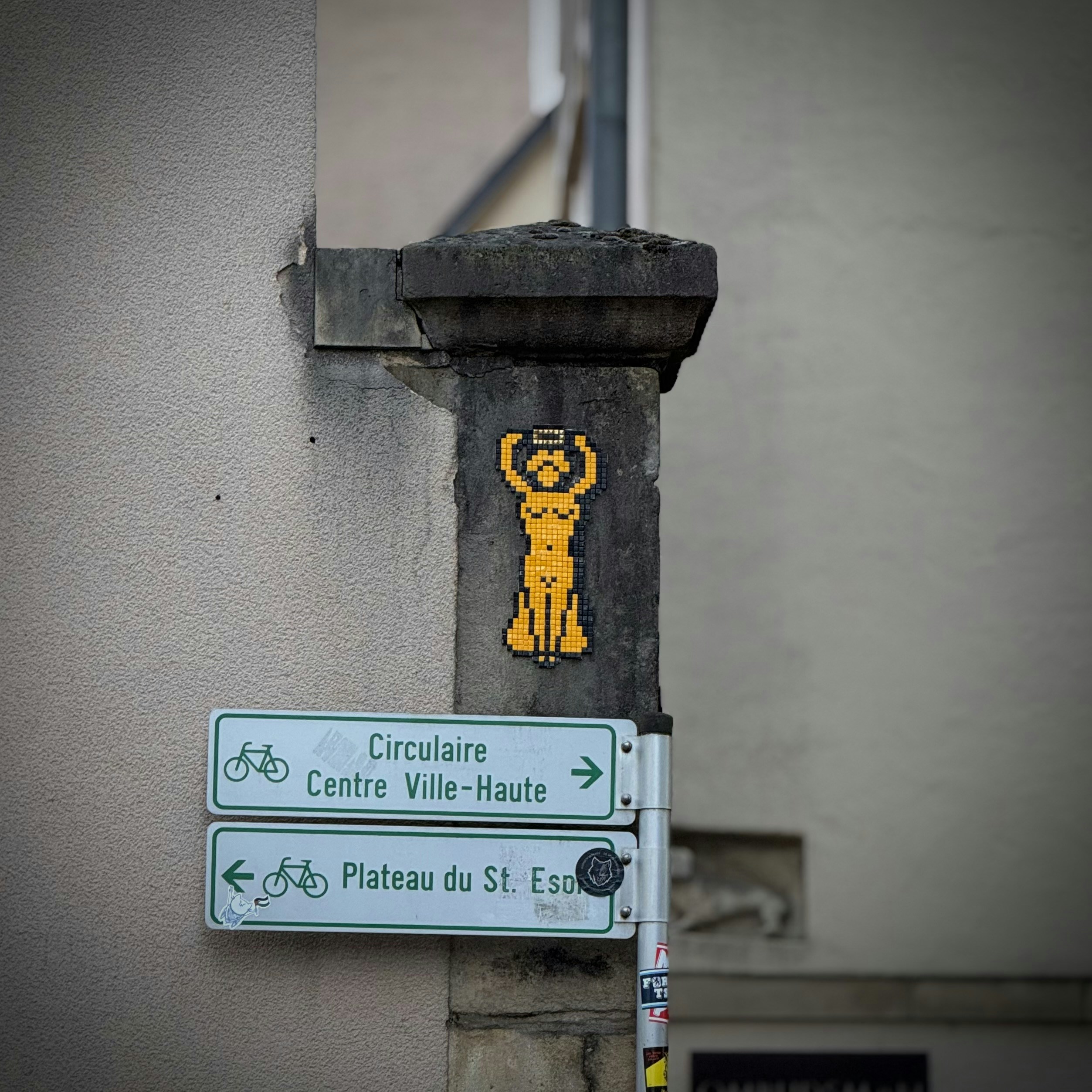 Pixelated yellow figure on a stone pillar near signs.