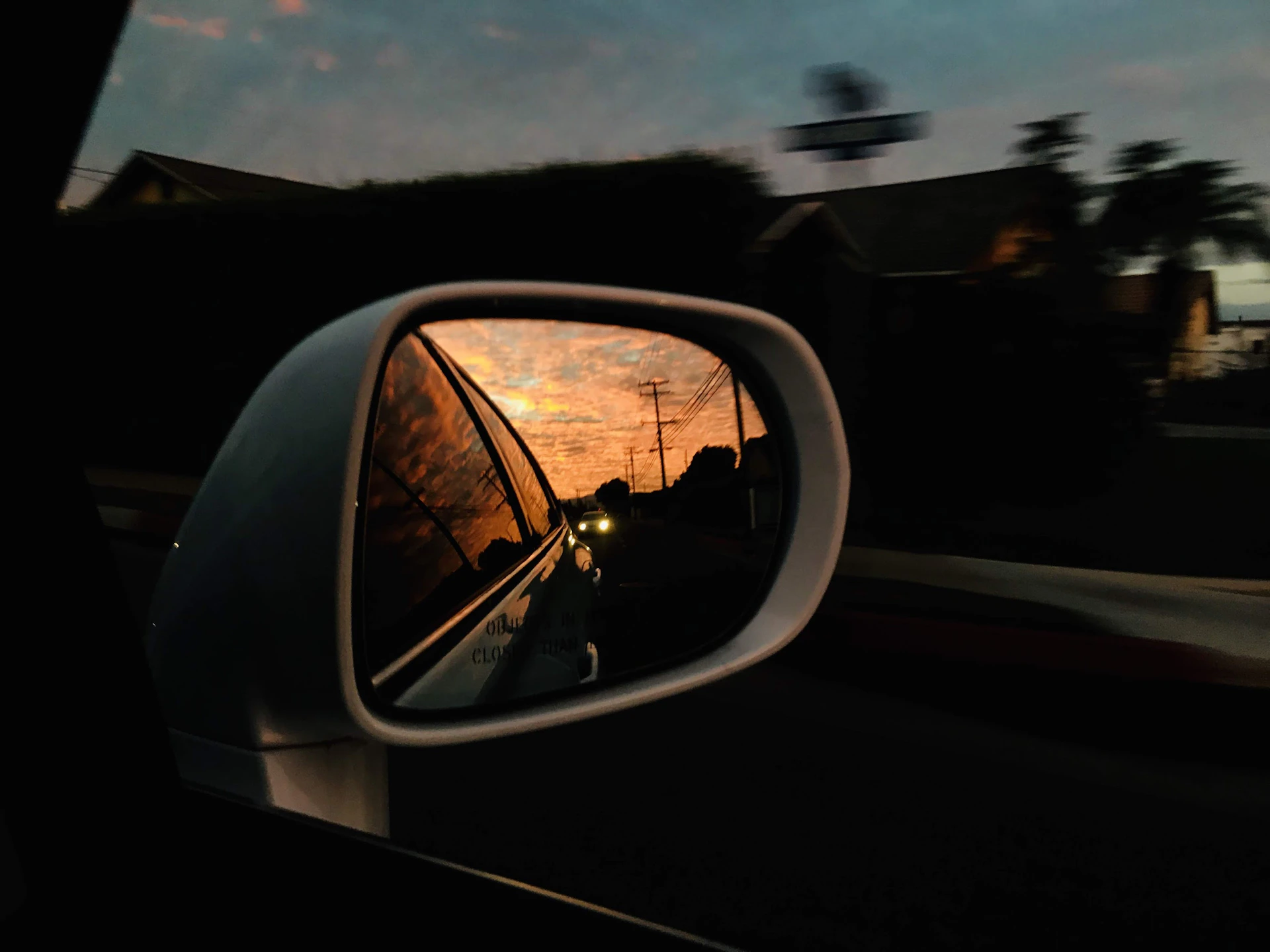 Car side mirror reflecting sunset over road.
